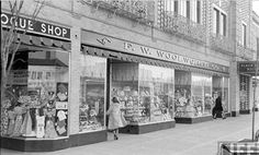 an old black and white photo of a woman walking down the street in front of a store