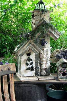 a bird house sitting on top of a wooden table next to a bucket filled with flowers