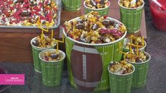 football themed cups filled with popcorn and marshmallows are sitting on a table