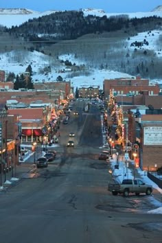 a city street with cars parked on both sides and snow covered mountains in the background