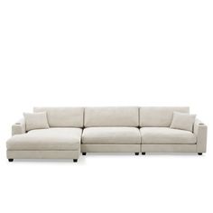 a white sectional couch with pillows on the top and bottom, in front of a white background