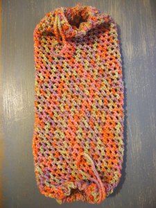 an orange and pink crocheted bag sitting on top of a wooden table next to a gray wall