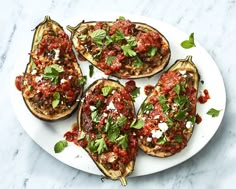 four stuffed eggplant halves on a white plate topped with sauce and parsley