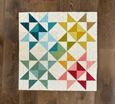 a multicolored quilt on a wooden floor with the colors of different shapes and sizes