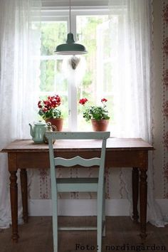 two potted flowers sitting on top of a wooden table next to a window with curtains