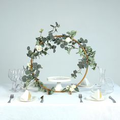 the table is set with white dishes and silverware, including an eucalyptus wreath centerpiece