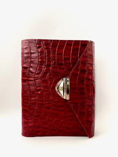 a red alligator skin notebook with a metal button on the front and an open cover