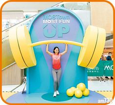 a woman standing in front of a giant sign with yellow balls around her and arms above her head