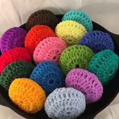 there are many different colored crocheted balls in a black bowl on the bed