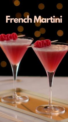 two martinis with raspberries in them sitting on a tray next to each other