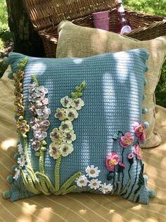 two pillows sitting on top of a bed covered in blue crocheted material and flowers