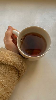 someone is holding a cup of tea in their hand with a towel on the table