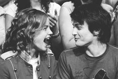 black and white photograph of two young men laughing at each other in front of a crowd