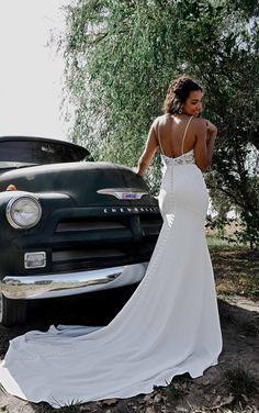 a woman in a wedding dress standing next to an old truck with her back turned