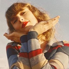 a woman with her hand on her face and hands clasped to her chest, standing in front of a blue sky