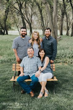 a group of people sitting on top of a wooden bench in the grass next to trees