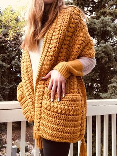 a woman wearing a yellow crochet cardigan and black leggings stands on a porch