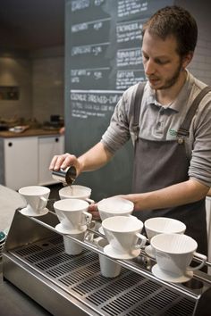 a man pours coffee into cups in front of a chalkboard