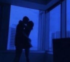 two people standing in front of a window with their arms around each other and kissing