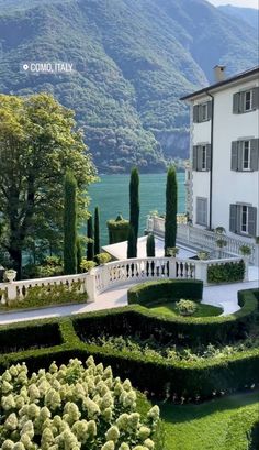 a large house surrounded by lush green trees and bushes in front of a body of water