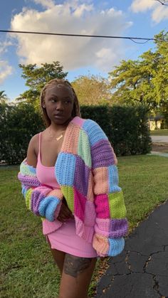 a woman standing in the grass with her arms around her body wearing a colorful sweater