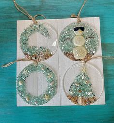 three glass ornaments are hanging from twine on a blue wooden table with white paper