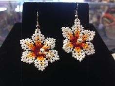 a pair of white and orange beaded earrings sitting on top of a black stand