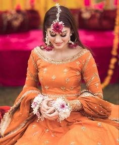 a woman in an orange dress with flowers on her head sitting down and smiling at the camera