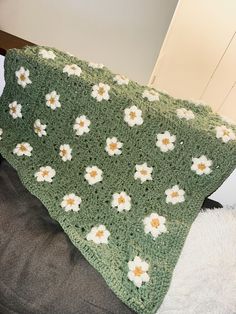 a green crocheted blanket with white and yellow flowers