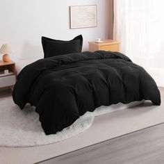 a bed with black comforter and pillows in a room next to a white rug