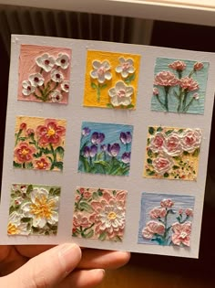 a person holding up a piece of paper with flowers painted on it in different colors