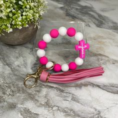 a pink and white beaded bracelet on a keychain next to a potted plant