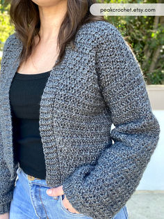 a woman standing in front of a tree wearing a gray knitted cardigan sweater