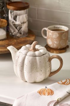 a white ceramic tea pot sitting on top of a counter next to a cup and saucer