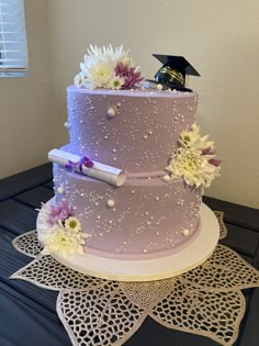 a purple cake with white flowers and a graduation cap on top is sitting on a doily