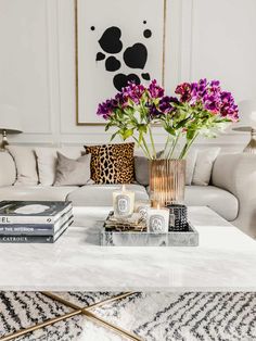 a living room filled with furniture and flowers on top of a coffee table in front of a painting