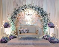 a white couch sitting under a chandelier covered in flowers and greenery on top of a carpeted floor