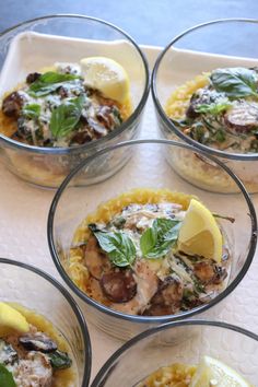 four glass bowls filled with food on top of a white tablecloth covered countertop