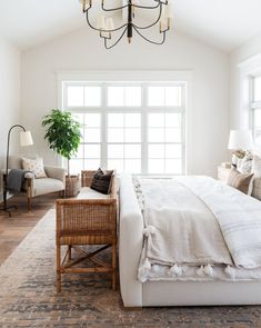 a bedroom with a bed, chair and chandelier hanging from the ceiling in front of two windows