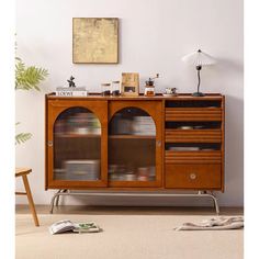 a wooden cabinet with glass doors and metal legs in a living room next to a plant