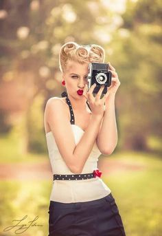 a woman holding up a camera in front of her face while wearing a white top and black skirt