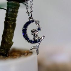 a silver necklace with an image of a mermaid sitting on the moon and holding a star