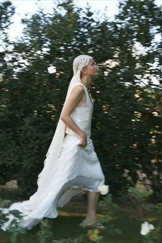 a woman in a white dress is walking through the grass