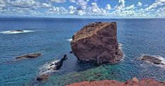 a large rock sticking out of the ocean next to some rocks and water with clouds in the sky