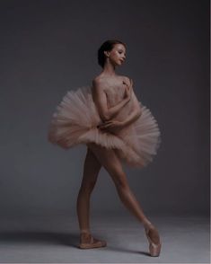 a ballerina in a pink tutu and ballet shoes posing with her arms behind her back