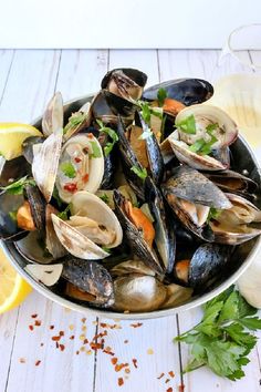 a bowl full of mussels and clams with lemon wedges