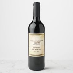 a bottle of red wine sitting on top of a white marble countertop next to a black and gold label