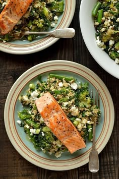 two plates with salmon, broccoli and feta salad on them next to silverware