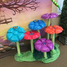 four colorful flower shaped candles sitting in front of a wall with a painting on it