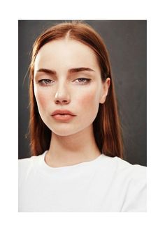 a woman with long brown hair and blue eyes wearing a white t - shirt is looking at the camera